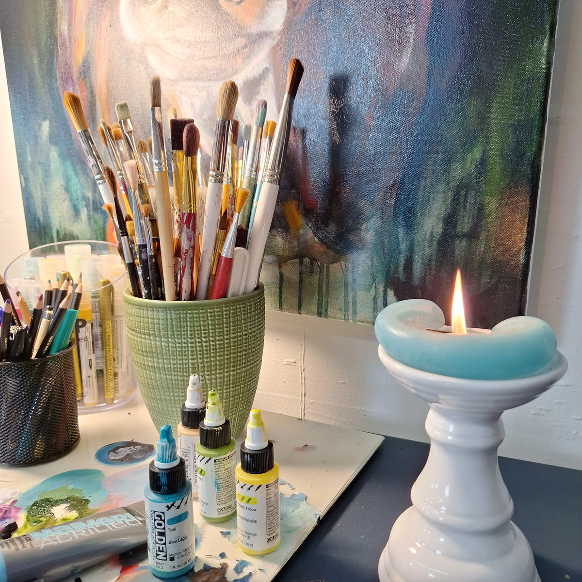 Art studio workspace with paintbrushes, paints, and candle