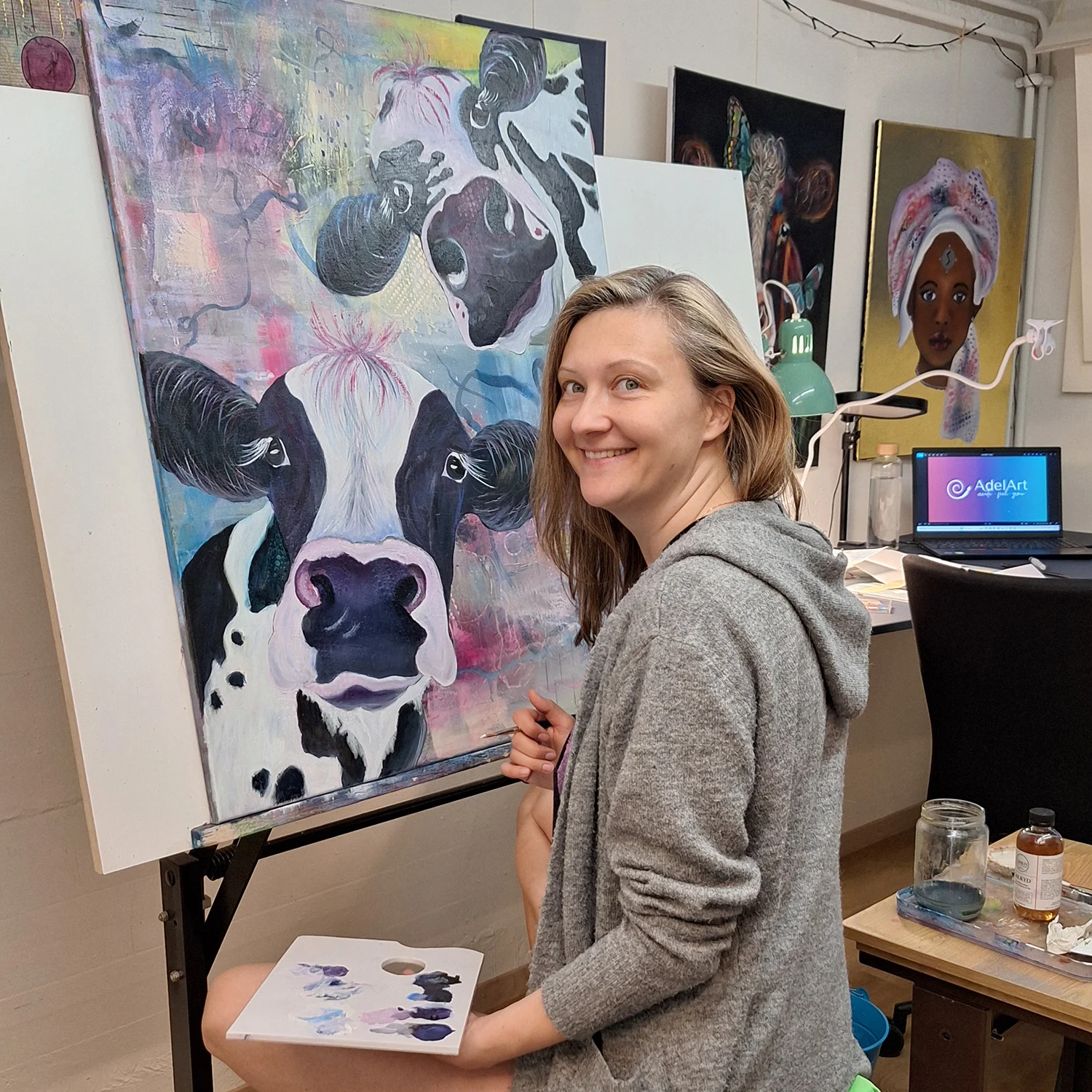 Adela smiling with her colorful cow painting in the studio
